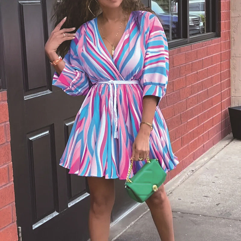 Woman in a colorful striped dress holding a green purse against a brick wall.