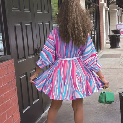 Person wearing a colorful dress with a pattern, standing on a sidewalk.