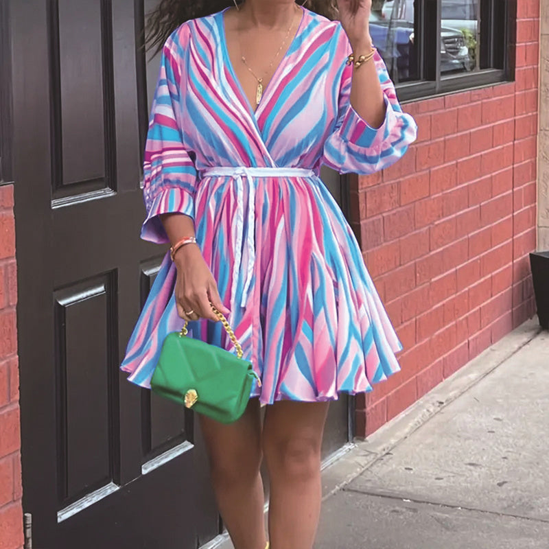 Person wearing a colorful striped dress holding a green handbag on a sidewalk.2