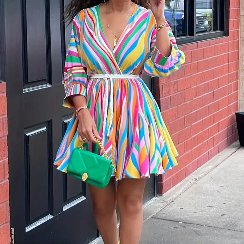 Person wearing a colorful striped dress with a green handbag against a brick wall.