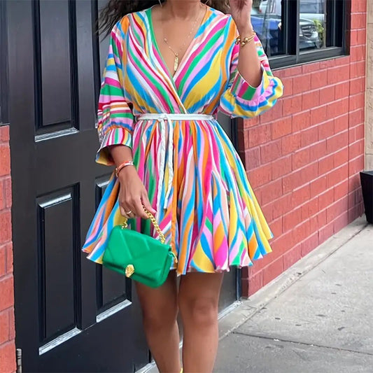 Person wearing a colorful striped dress with a green handbag against a brick wall.