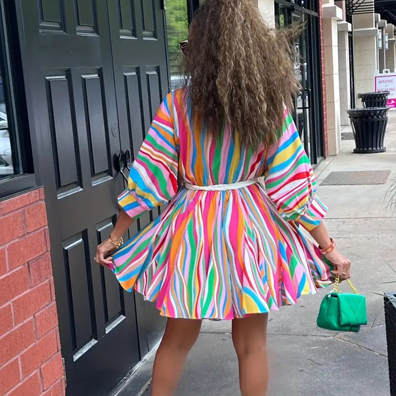 Person wearing a colorful striped dress standing on a sidewalk.