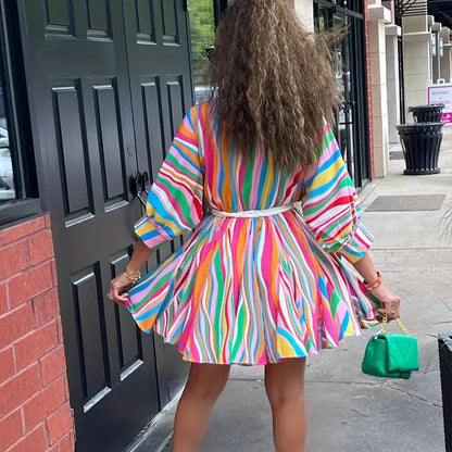 Person wearing a colorful striped dress standing on a sidewalk.